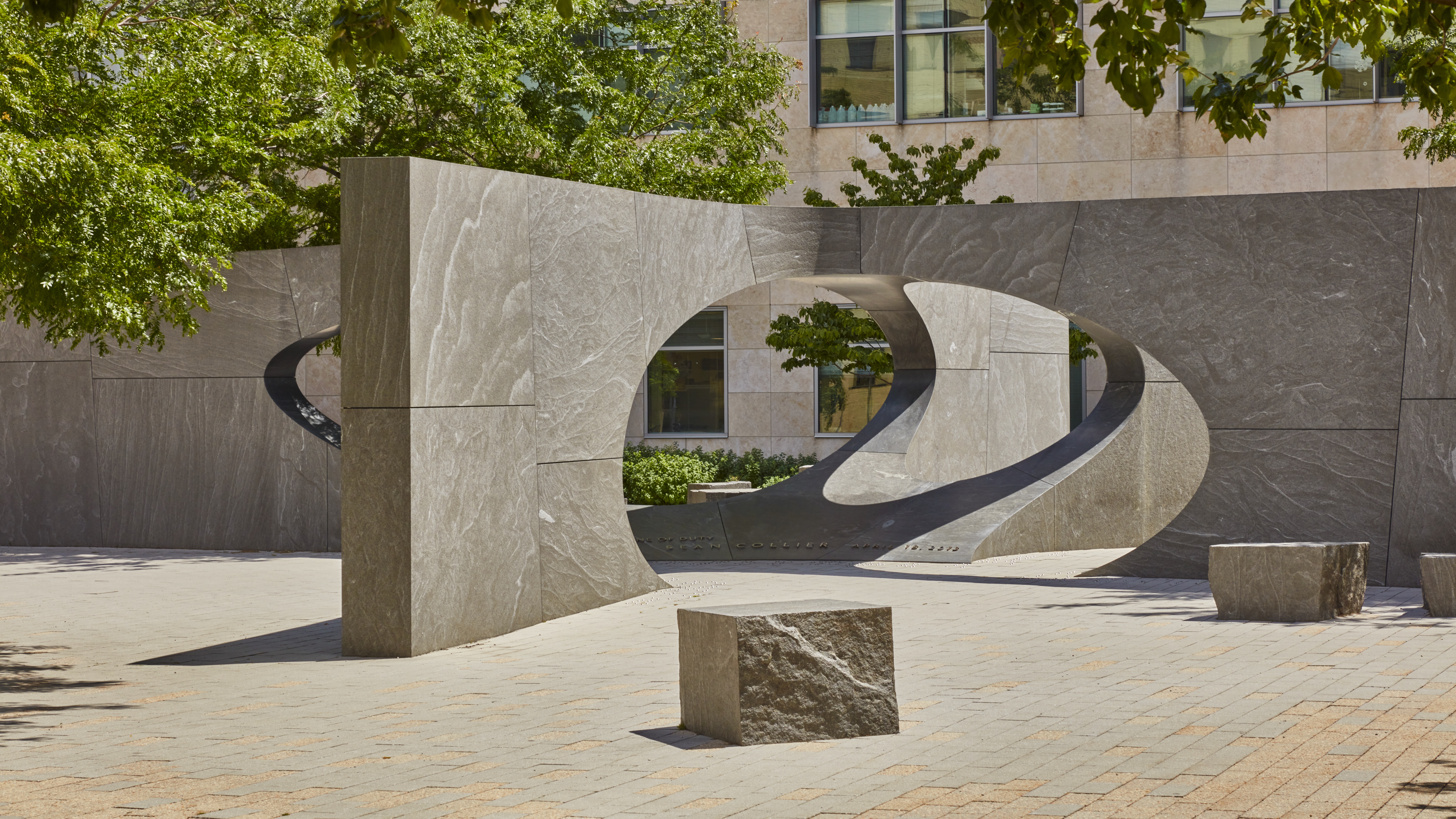 Granite open air sculpture featuring a rectangular shape with ovals cut out in the middle surrounded by trees peaking through the top edge of the photo.