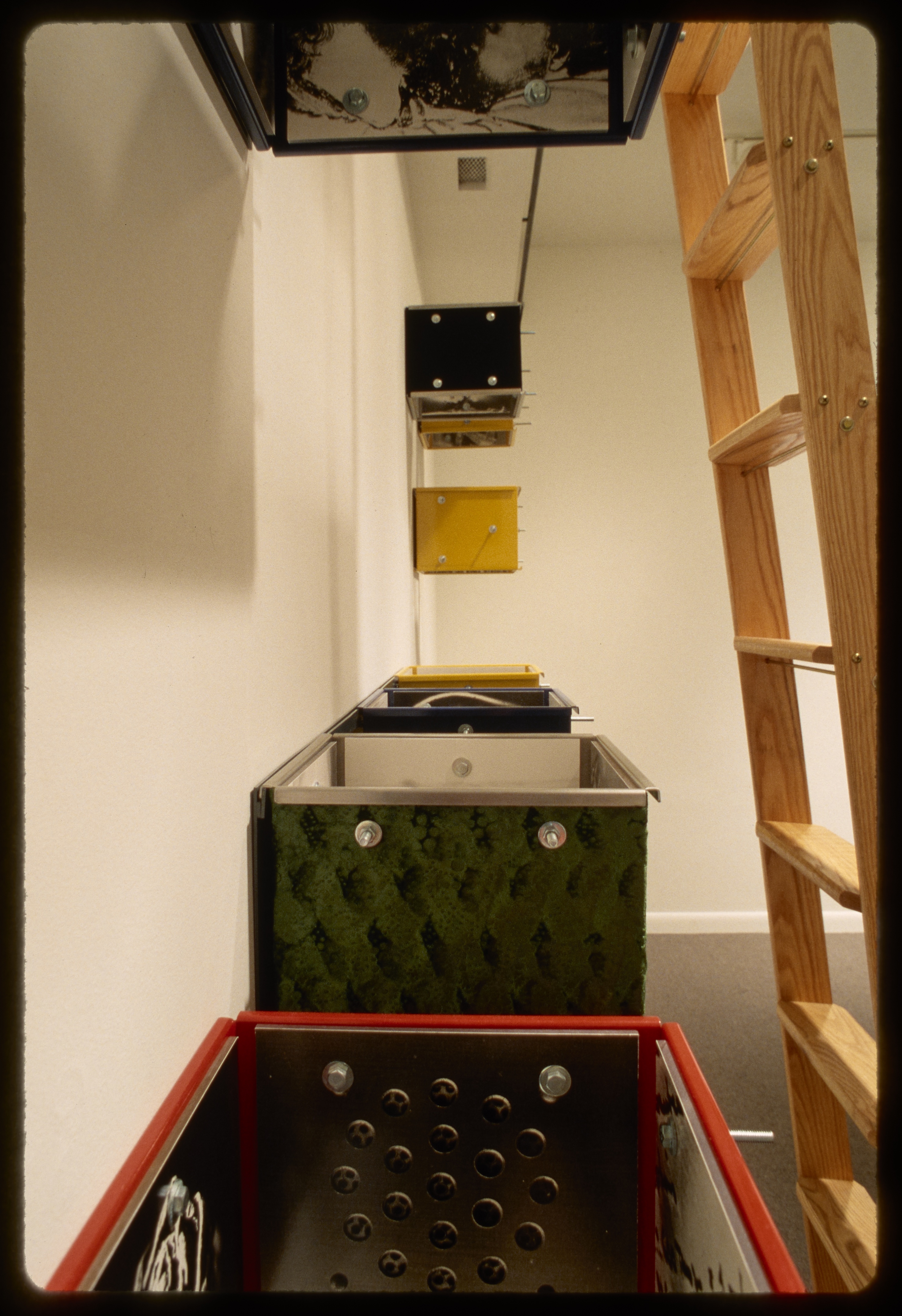 Eight colorful boxes without tops or bottoms are lined on the inside with metal sheets with holes and white and black photos.