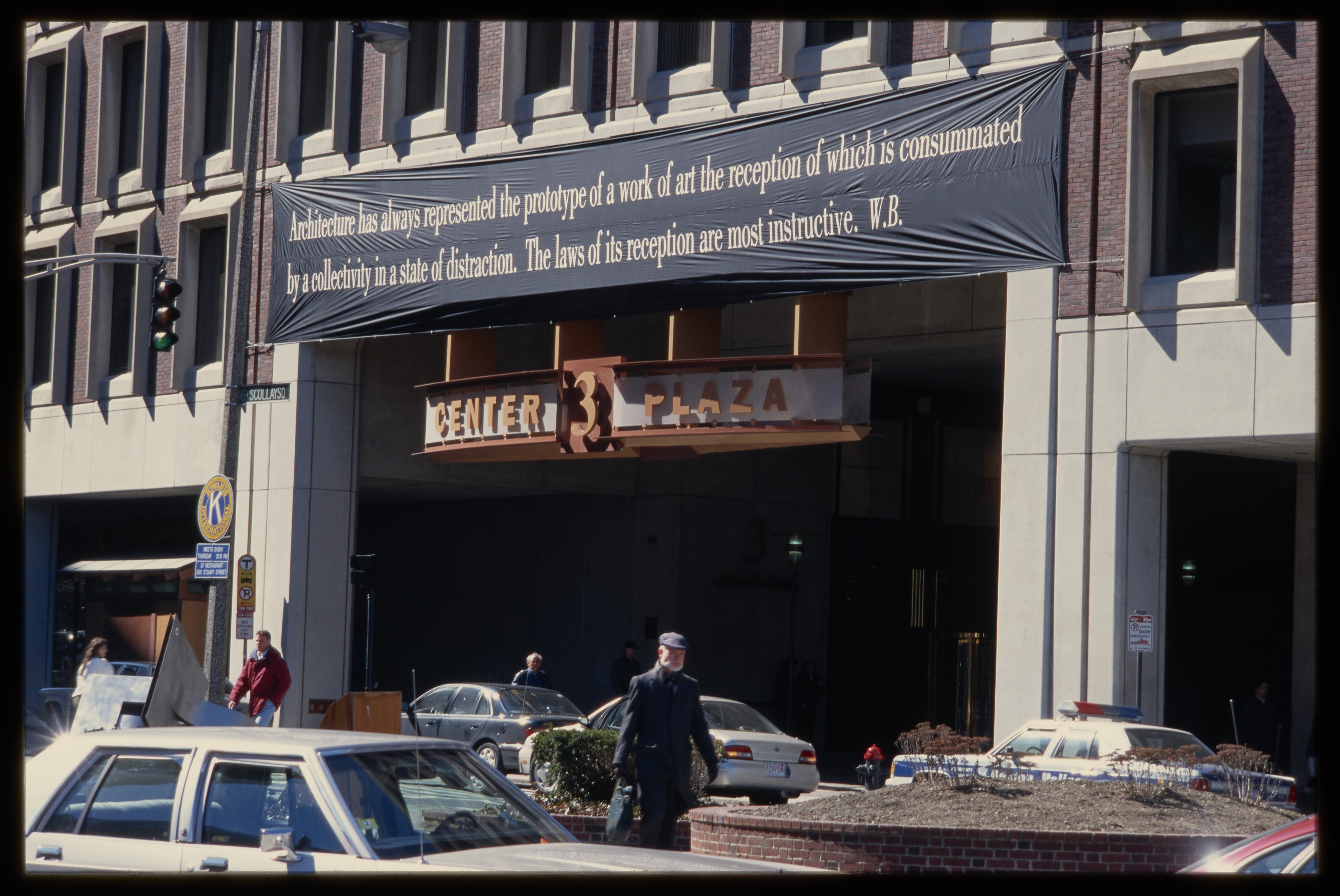 A long black banner, displaying a quote in white text, hangs over the entry of an office building on a busy city street.