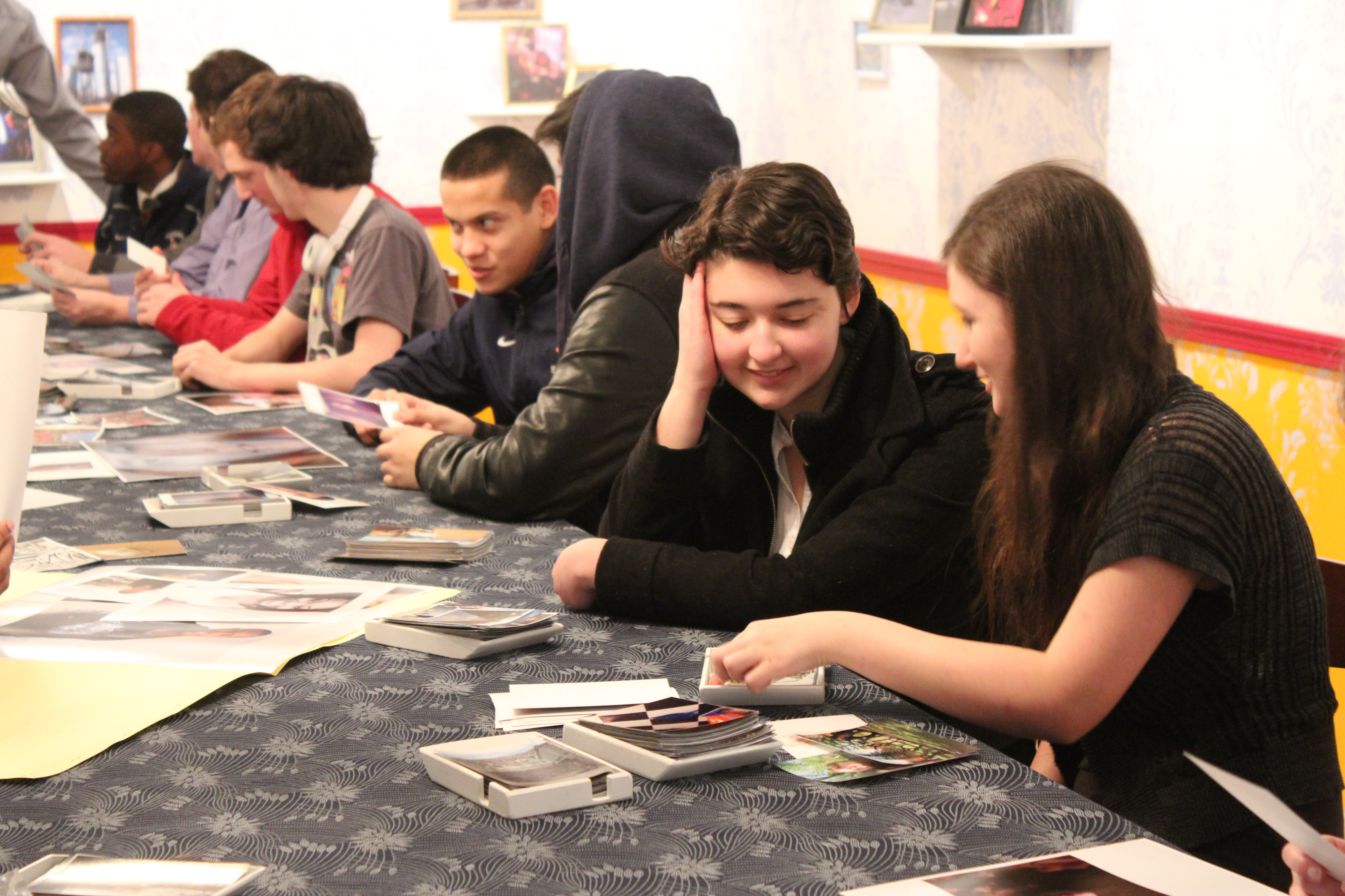 High school students sit at one side of a long table looking at photos, talking to each other in pairs.