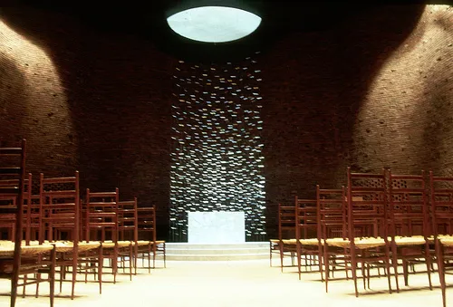Installation view of a steel hanging sculpture in a chapel lined with wooden chairs.