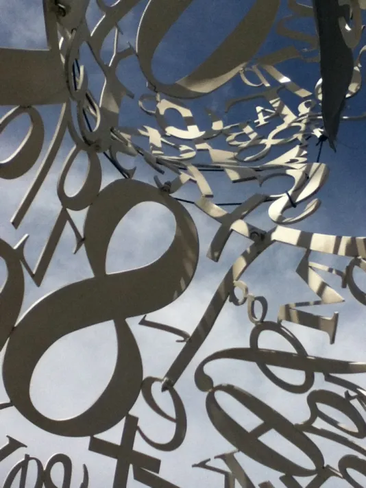 Sculpture made of tainless steel, white enamel paint featuring collages of letters, numbers, or symbols that appear to be in the process of organization.