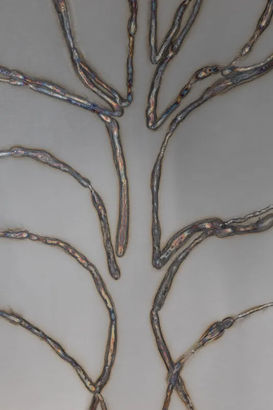 Detailed view of welded steel with two vertical lines that have branch-like shapes coming out on the left and right of the lines forming a shape that resembles a tree.
