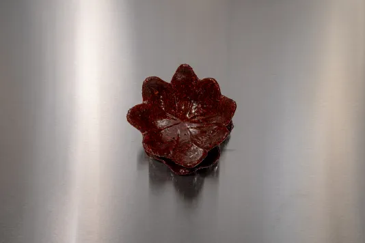 View from above of a deep red bukhoor incense cast in the shape of a water lily on a silver steel table. 