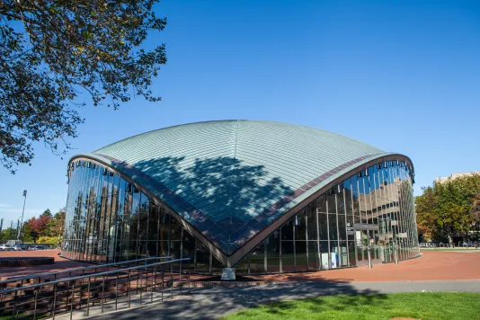 Oval shaped building with around top that has a point that goes to the ground and has glass siding. 