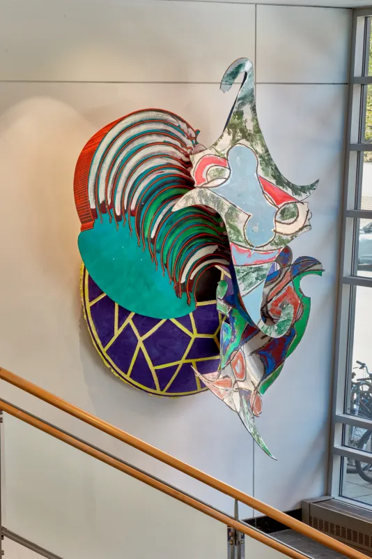 Colorful sculpture made of acrylic and enamel on aluminum hung on a white wall. 