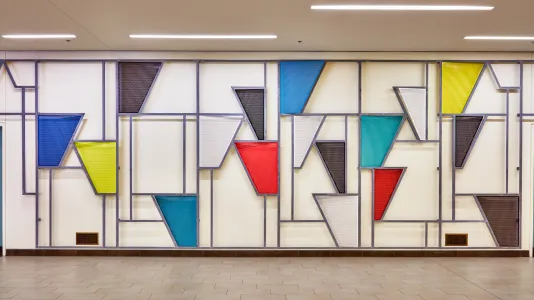 Painted steel sculpture on a wall featuring triangular shapes and lines.
