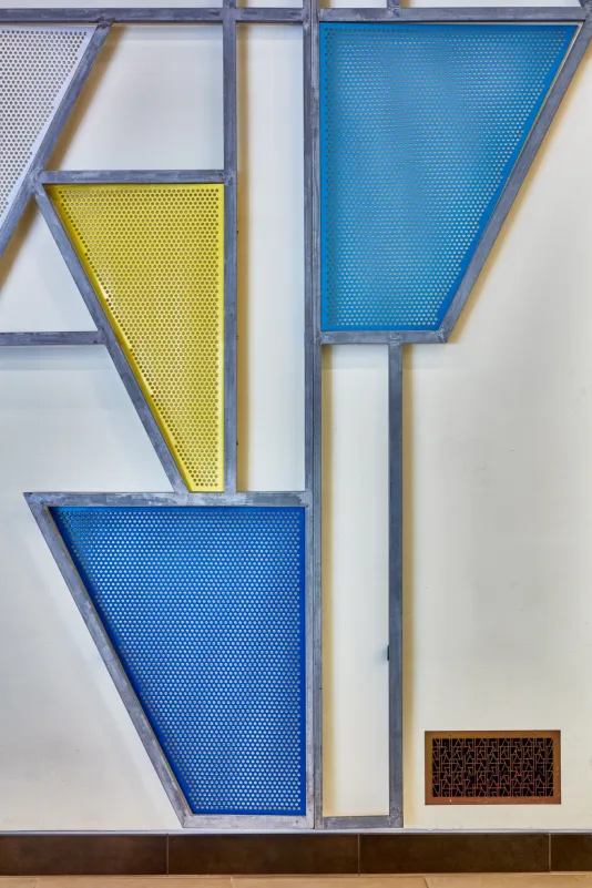 Close up of a steel sculpture with blue and yellow geometric shapes against a wall. 