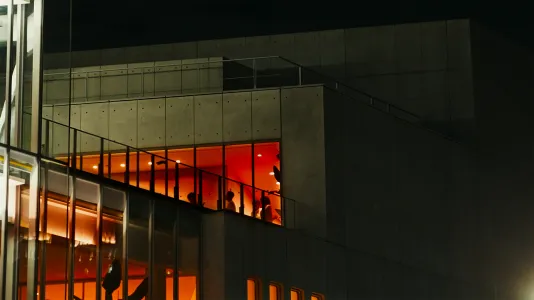 : Through windows on the Brutalist façade of Renzo Piano-designed [building], visitors move through orange-hued galleries. Still from history as hypnosis