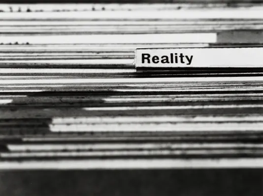 Detail image of many file folders in a row. There is one label tab highlighted with black bolded text. The text reads "Reality"