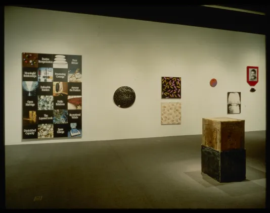 Two stacked boxes sit in front of wall with seven artworks of various sizes and shapes.