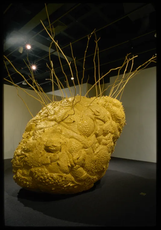 A large bright yellow sculpture shaped like a lemon with a coarse textured surface and protuberances sticking out of the top.