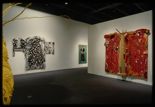 2 abstract paintings resemble Kimonos hung on walls. 1 is black and white, another is red with a wood column in the middle.