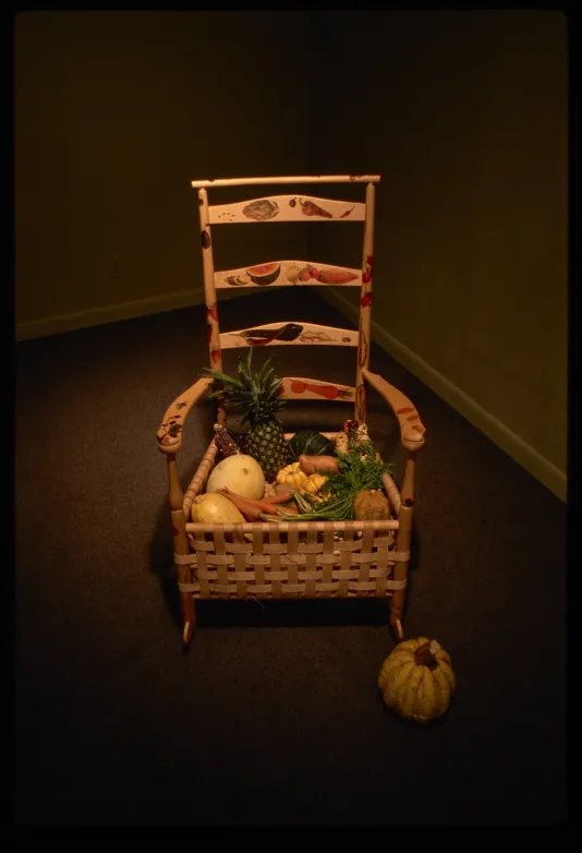 17th or 18th century chair adapted with the seat as a basket, fruit painted on the back and arms, filled with fruit, with squash on the ground next to it. 