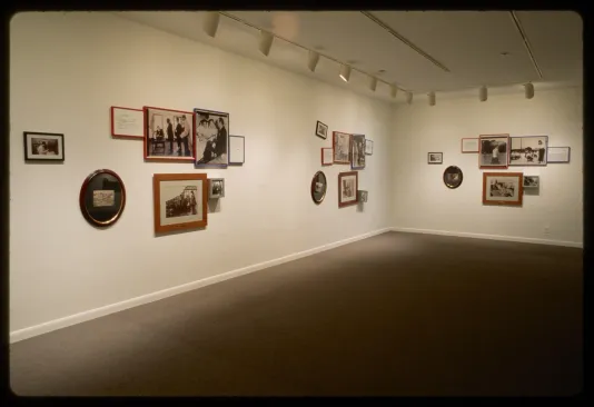 Three groups of eight framed black and white photos of different shapes and sizes hang on adjacent gallery walls. 
