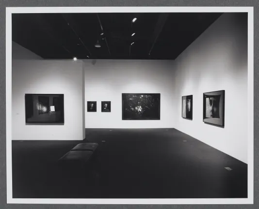 Photographs of different sizes line the gallery walls. A bench is in the center of the gallery for viewing the works. 