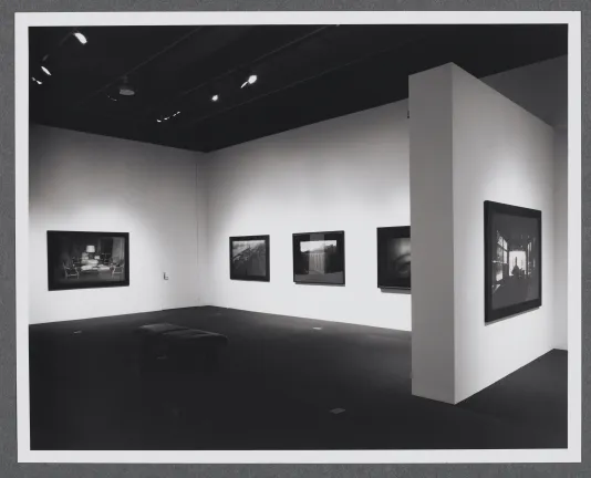 Photographs of different sizes line the gallery walls. A bench is in the center of the gallery for viewing the works.
