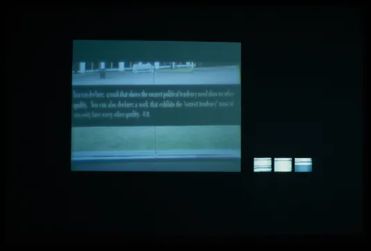 In a dark room, a large screen displays a banner of text over a bluegreen image. 3 small active monitors sit beside it.