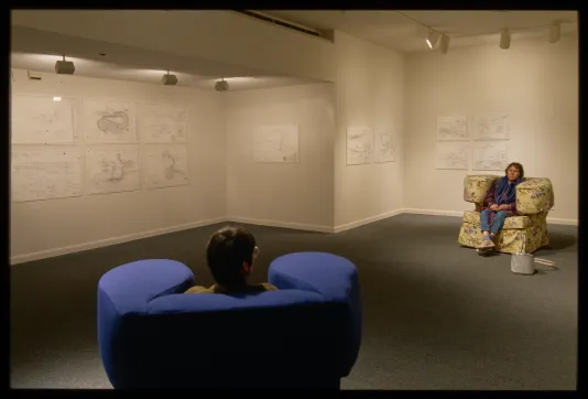 Two cushioned chairs are set across from each other. Each face a wall with technical drawings of the chair designs.