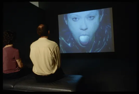 Large video scree with a close up af a young woman sticking out her tounge. 
