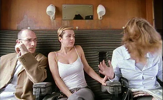 Two train passengers, a man and woman, look on at a third passenger, a frantic woman with hair in her face in a video still