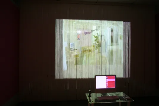 An image is projected onto a wall covered with fringe, distorting the picture. In front of the projection is a Mac monitor with a chat box open.