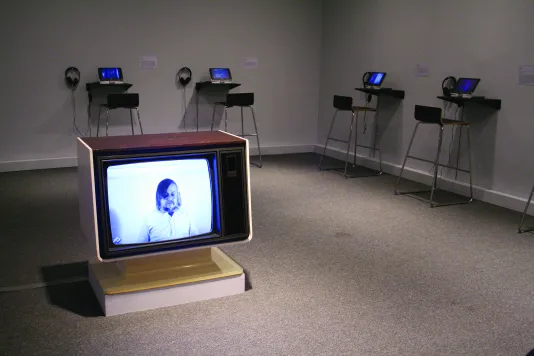 Small TV sitting on the floor of a gallery with an image of a man on the screen.