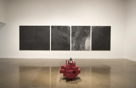 4 paneled large, abstract, grey painting with red brick sculpture in the foreground.