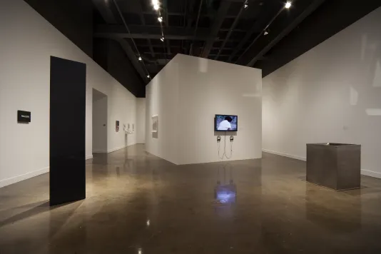 A space with a tall, black monolith, a white structure with a video monitor on the outside, a brown rectangular box