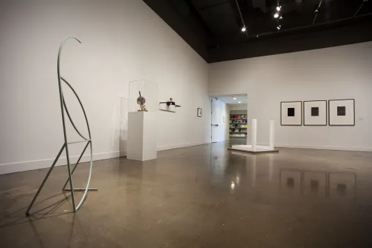 A delicate metal sculpture, a stand with an object, framed pictures and floor sculpture with white base, two white poles