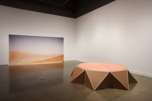 A canvas printed with a desert vista spills onto the floor; nearby is a circular stage, its base made of triangular shapes.