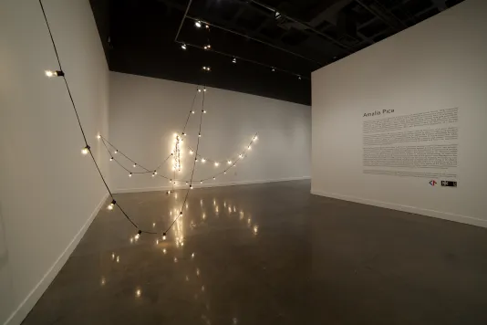 A long line of illuminated bulbs strung from a high ceiling and at 4 separate points on two walls, reflect off a glossy floor.