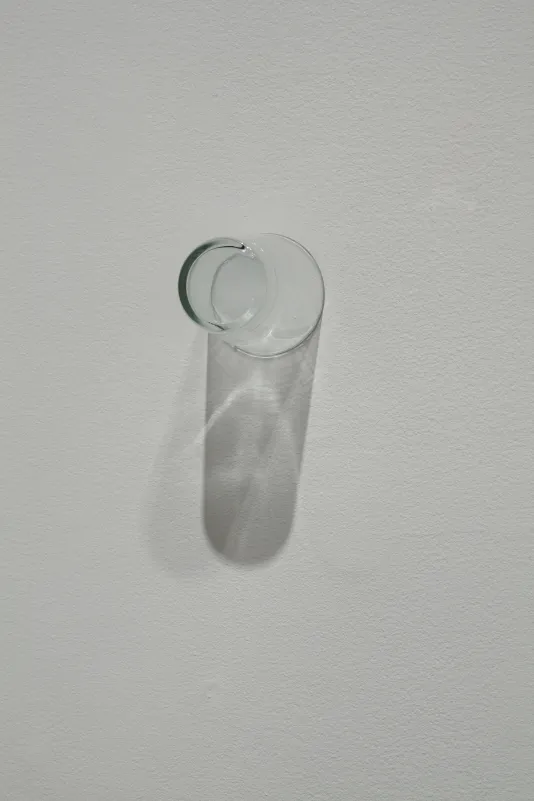  A clear drinking glass is affixed on a wall by its rim.