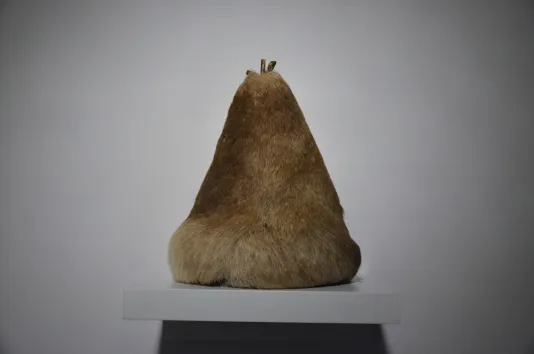 A mound of tan-color reindeer hair in the shape of a pear displayed on a white wall-mounted shelf