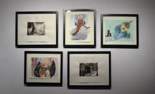 Five framed watercolor paintings that appear to have been created with a childlike style are arranged on the wall.