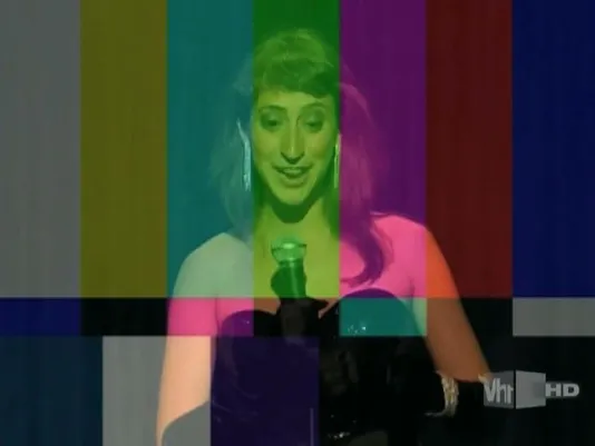 An overlay of yellow, green, pink, red and blue stripes color the image of a young woman in formal wear speaking into a mic.