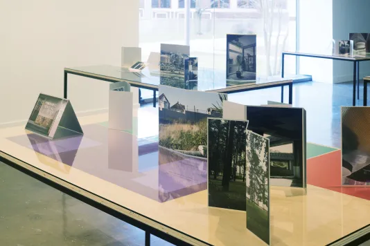 Installation view of table tops with photographs and color gels in front of a picture window letting light in from outside