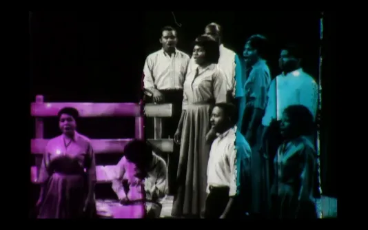 Vintage video still of a black choir, the original black and white footage overlaid with a purple and blue wash of color.