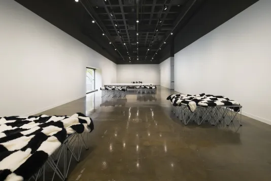 A series of platforms draped with checkered blankets, seen in a long view of a gallery.