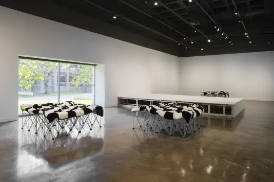 Three metal stages covered in black and white blankets in a gallery space, along with a low white wooden stage.