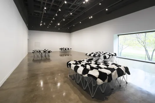 Long view of a gallery space displaying four separate small stages draped with black and white checkered blankets.