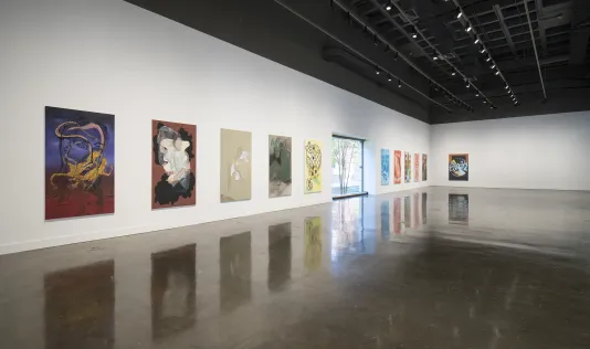 A gallery wall is lined with paintings by a gallery window.