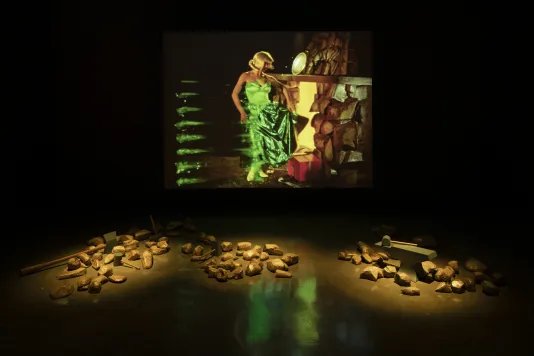 Three piles of gold rocks are placed in front of a screen on which a woman in a green dress stands in front of a hearth.