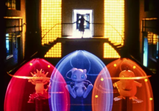 Video still showing a woman standing at the top of a double staircase, while 3 animated creatures float in colorful pods.