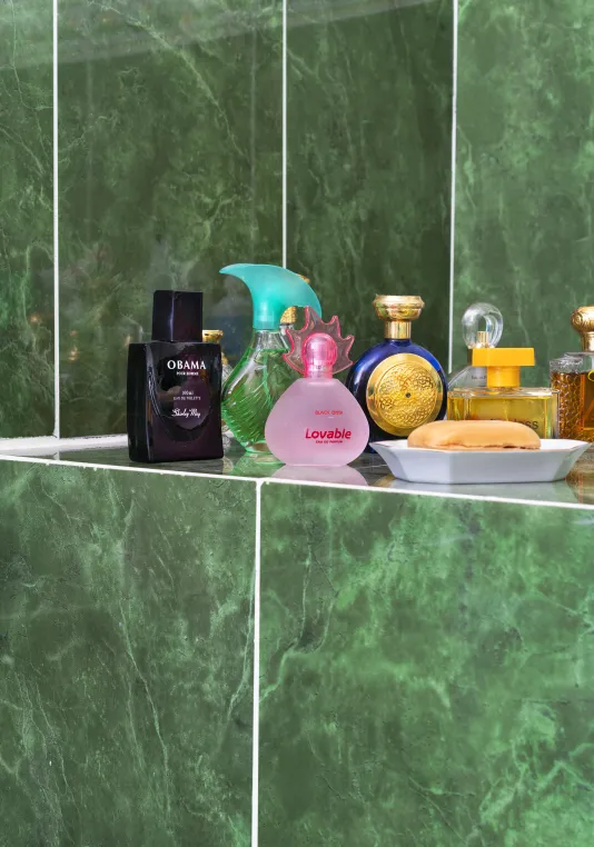 Perfume bottles, a black 1 labelled “OBAMA”, a pink 1 “LOVABLE” with others in blue and gold against green stone-pattern tile