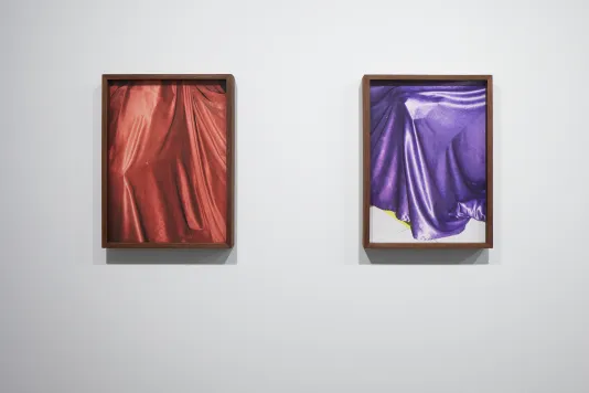 Photo of shiny red draped fabric hangs next to a photo of shiny purple draped fabric with hem falling on white tiled floor.