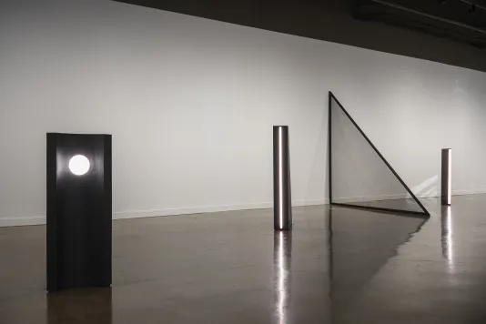 Three black standing sculptures, each with a different light, and a large black mesh triangle jutting from the wall.