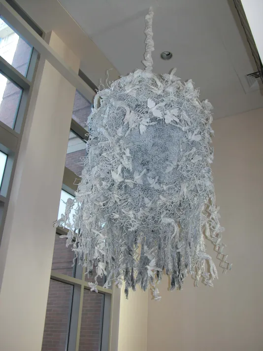 Sculpture hanging from a ceiling made of wax, wire mesh, found objects, and mixed media
