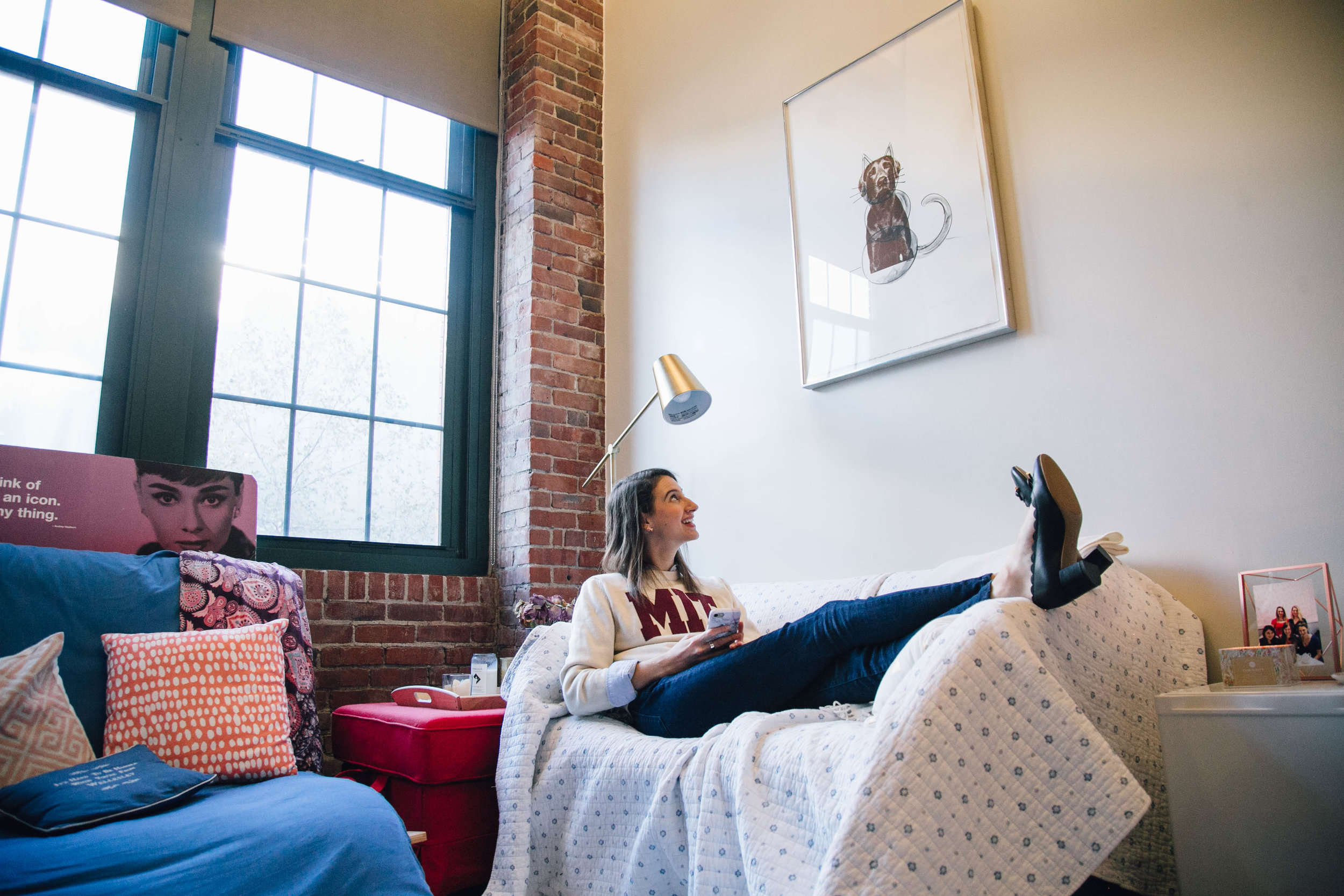 Woman lies on her couch in her apartment looking up at a print on the wall to her left.