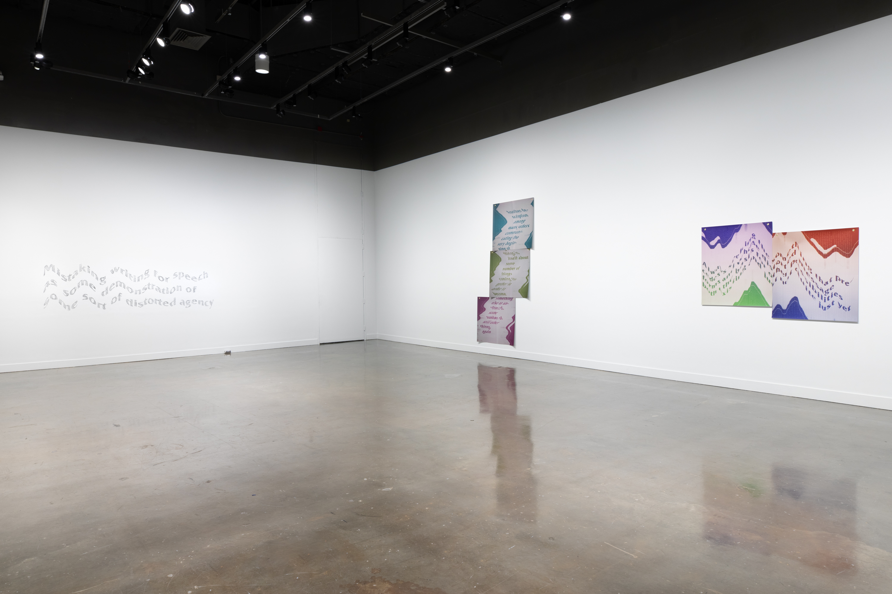Installation view featuring a set of three inkjet prints on vinyl on a wall next to two prints side by side and a gray text mural on the far-left wall.